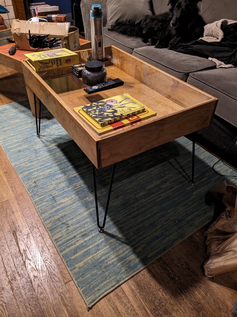 a finished wooden table with hairpin legs and a goofy dog laying on a couch